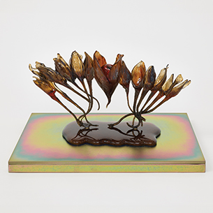 A glass sculpture depicting a series of organic, flower-like forms arranged in an arc. The sculpture is mounted on a colorful, iridescent base.